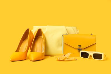 Şık çantalı sarı topuklu, güneş gözlüklü ve arka planda sonbahar yapraklı.