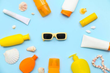 Mavi arka planda güneş kremi, güneş gözlüğü ve deniz kabukları olan kompozisyon