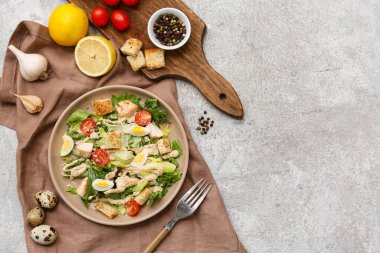 Lezzetli tavuklu Sezar salatası ve gri arka planda malzemeler.