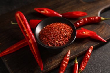 Siyah arkaplanda kırmızı biber tozu olan kase, yakın plan.