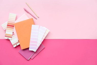 Pembe zemin üzerinde farklı boya paletleri, kitaplar, kalem ve kalem içeren kompozisyon