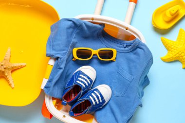 Çocuk bavulu, giysiler, plaj aksesuarları ve mavi arka planda oyuncaklar, yakın plan.