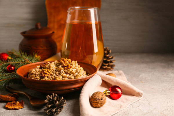 Bowl of traditional Ukrainian Kutya dish with fir branch, Christmas balls and jug of uzvar on white table