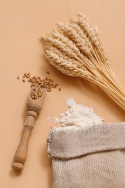 Bir torba buğday unu, tahıllı ahşap kepçe ve bej arka planda dikenli dikenler.