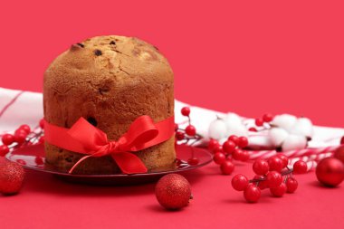 Lezzetli Panettone tabağı ve kırmızı arka planda Noel dekoru.