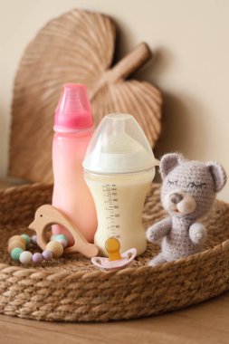 Ağaç mutfak tezgahında bebek sütü formülü şişeleri ve oyuncaklarıyla hasır tepsi, yakın plan.