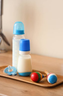 Bebek sütü formülü şişeleriyle dolu tepsi, duvarın yanındaki ahşap masada çıngırak ve emzik.