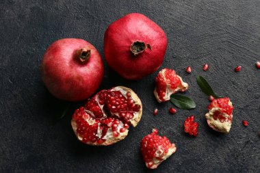 Koyu arkaplanda tohum ve yapraklarla taze olgun nar.