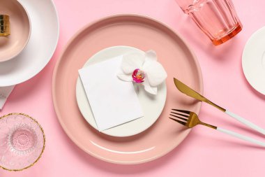 Altın çatal bıçak takımı ve pembe arka planda orkide çiçeğiyle güzel bir masa.