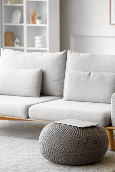 Laptop on grey pouf in living room interior