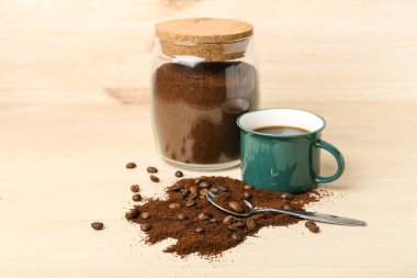 Bir kaşık kahve tozu, fasulye, kahve fincanı ve kavanoz açık ahşap masada.