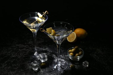Lezzetli martini, buz küpleri, yeşil zeytin ve koyu arkaplanda limon.