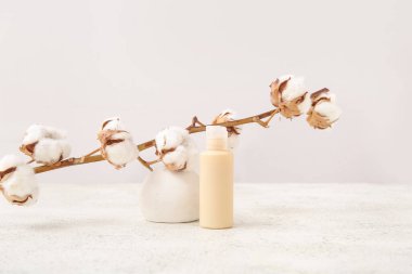 Hafif arkaplanda bir şişe kozmetik ürünü, sıva podyumu ve pamuk dalı