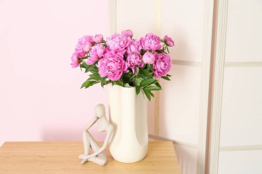 Rafların üzerinde pembe şakayık ve biblo vazosu ve renk duvarına yakın giyinme ekranı var.