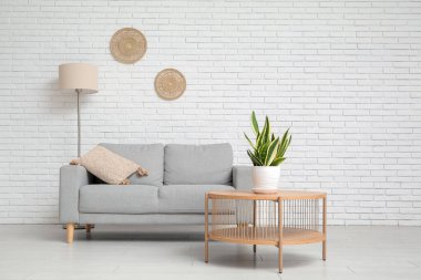 Beyaz tuğla duvarın yanında kanepesi, masası ve bitkisi olan oturma odasının içinde.