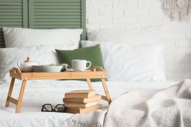 Kahvaltı tepsisi, kitap ve gözlük odada.