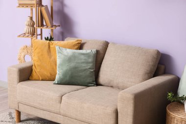 Oturma odasında eflatun duvarın yanındaki yastıklı gri kanepe.