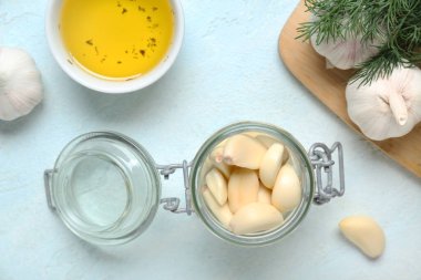 Taze sarımsaklı kavanoz ve açık mavi arka planda bir kase yağ.