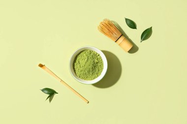 Yeşil arka planda pudralı kibrit çayı, taze yapraklar, chasen ve chashaku.