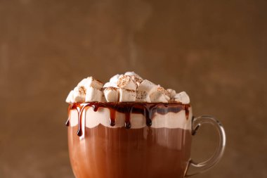 Kahverengi arka planda krem şantili ve marşmelovlu bir bardak sıcak kakao, yakın plan.