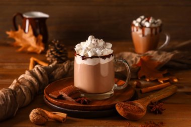 Bir bardak sıcak kakao, çırpılmış krema ve ahşap arka planda marşmelov.