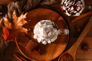 Cam bardaklarda krem şantili sıcak kakao ve ahşap arka planda marşmelov.