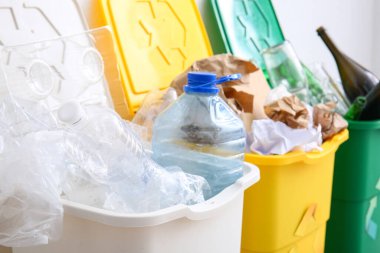 Geri dönüşüm sembollü çöp kutuları ve beyaz duvarın yanındaki farklı çöpler.