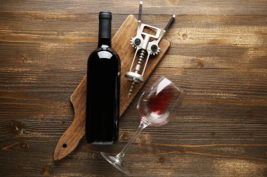 Ahşap zemin üzerinde kırmızı şarap şişesi, cam ve açacağı olan tahta.