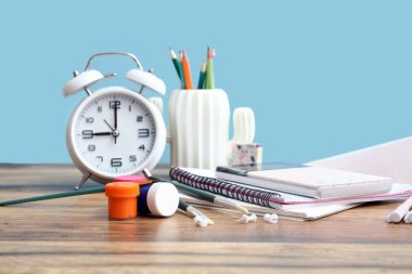 Renk duvarına karşı ahşap masadaki farklı kırtasiye ve alarm saati.