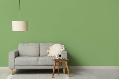 Asılı lamba, rahat bir kanepe ve içinde insan figürü ve dergi olan bir sehpa.