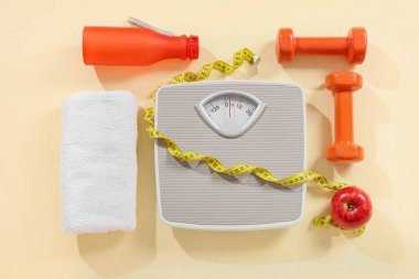 Bej arka planda mezura, elma ve dambıl ile ölçülmüş pullar. Kilo verme konsepti