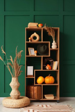 Yeşil duvarın yanında balkabağı, kitap ve dekor olan raf ünitesi.