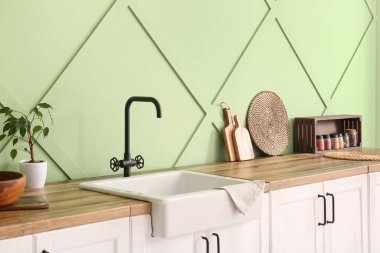 Mutfaktaki yeşil duvarın yanındaki tahta tezgahta beyaz seramik lavabo.