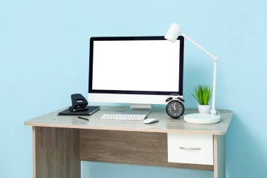 Rahat ofisteki mavi duvarın yanında bilgisayar, ev bitkisi ve lamba bulunan şık bir iş yeri.