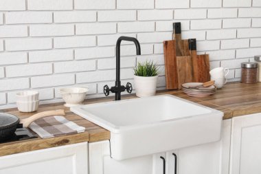 Beyaz lavabo, doğrama tahtası ve mutfak aletleri beyaz tuğla duvarın yanında. Yakın çekim.