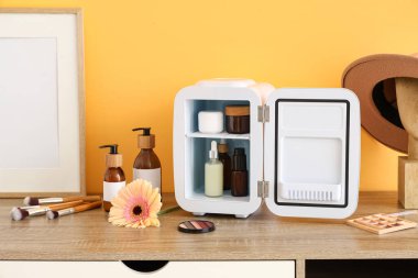 Küçük kozmetik buzdolabı olan masa, oda sarı duvarın yanında çerçeve ve çiçek. Yakın çekim.