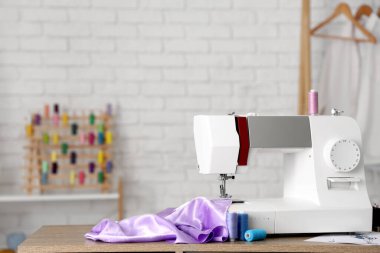 Atölyede eflatun kumaş ve ipliklerle modern dikiş makinesi.