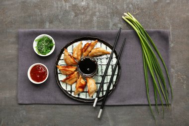 Bir tabak kızarmış Japon gyozası, bir kase sos ve siyah arka planda yosun salatası.