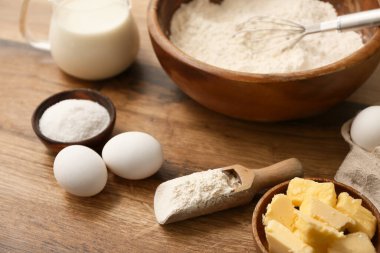 Tahta arka planda hamur hazırlamak için bir kase un, yumurta ve tereyağı.