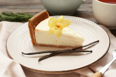 Vanilya çiçekli tatlı peynirli kek dilimi ve ahşap arka planda çubuklar.