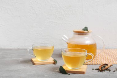 Bardaklar ve çaydanlık sıcak yeşil çay. Gri masa üzerinde kurumuş yapraklar.