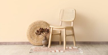 Rahat ahşap sandalye, puf ve bej duvarın yanında kurutulmuş çiçek vazosu.