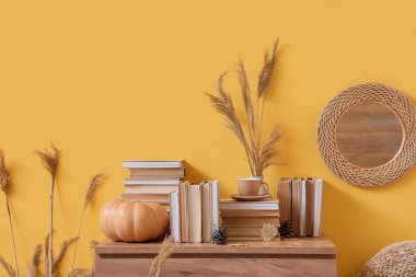 Sonbahar dekorasyonlu çekmeceler, balkabağı ve sarı duvarın yanında kitaplar.