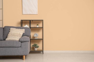 Bej duvarın yanında rahat kanepesi ve raf ünitesi olan şık bir oturma odası.