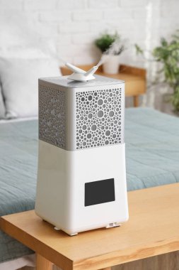 Yatak odasının içinde, yatağın yanındaki ahşap bankta modern nemlendirici var.