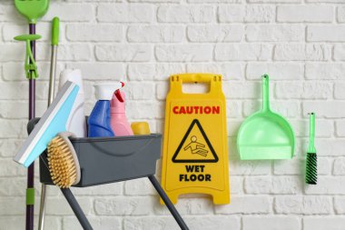 Bir sürü temizlik malzemesi ve uyarı levhası olan tramvay, beyaz tuğla duvarın yanında, yakın plan.