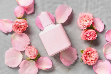 Bir şişe parfüm, güzel pembe güller ve gri arka planda suda yapraklar.