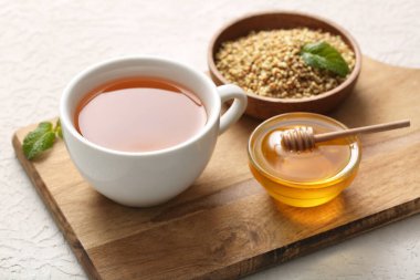 Bir fincan sıcak karabuğday çayı, ballı kase ve beyaz arka planda nane yaprakları.