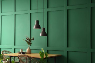 Okaliptüs dallı vazo ve yemek masasında yeşil duvarın yanında temiz tabaklar.