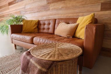 Oturma odasının iç tarafındaki ahşap duvarın yanındaki yastıklı kahverengi kanepe.